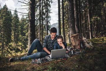 Fototapeta premium A couple of tourists lie on the blanket and looking at laptop in the woods. The concept of active rest