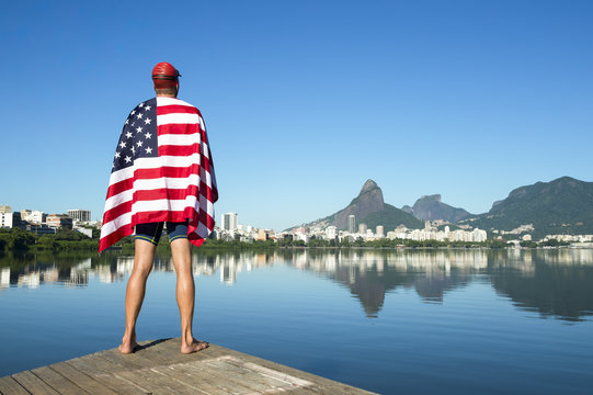Swimmer draped in American flag standing at Lagoa Rodrigo de Freitas Lagoon with a view of Rio de Janeiro skyline with Two Brothers Mountain