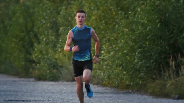 Road runner man running in park at dusk, slow-motion