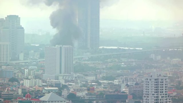 Thick, black clouds of smoke billow from the upper floors of a highrise building on fire in Bangkok, Thailand. Video UltraHD