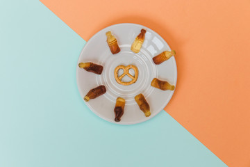 Stylish set: pretzel and jelly in shape of bottles on sauser on pastel blue and orange backgrounds. Flat lay. Top view.
