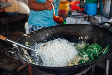 Woman cooks stir-fried noodles with bean sprouts