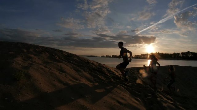 A group of athletes - two girls and a guy are fleeing the mountain, near river at dusk, slow-motion