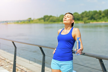 Young fit woman resting after jogging by the river in city.