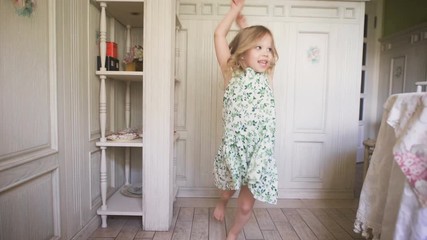 Happy blonde girl in the dress having fun dancing indoors in a sunny white room at home or kindergarten