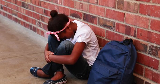 Sad pupil sitting alone in corridor