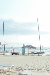 Light sunbeds, loungers, surfboard and beach umbrellas on empty sand beach
