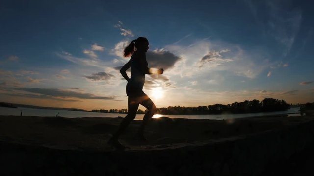 Running young woman in park at sunset, slow-motion, hands in a fist, silhouette