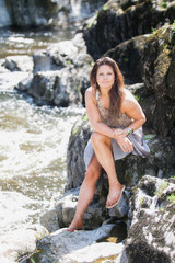Beautiful young lady sat on rocks by a river