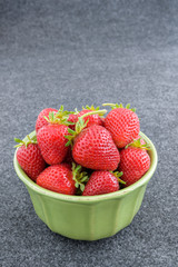 Fresh picked strawberries in a green bowl on a gray background
