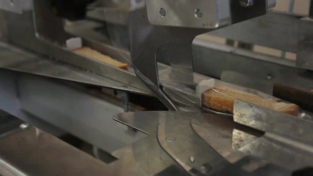 Automatic packaging of bread in plastic on a conveyor belt closeup.