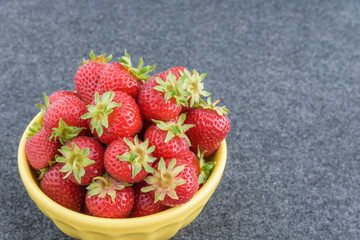 Fresh picked strawberries in a yellow bowl on a gray background
