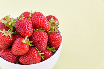 Fresh picked strawberries in a white bowl on a light green background
