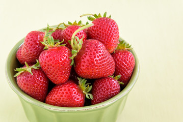 Fresh picked strawberries in a green bowl on a light green background
