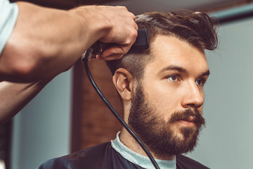The hands of young barber making haircut to attractive man in barbershop