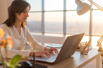 Side view photo of a female programmer using laptop, working, typing, surfing the internet at...