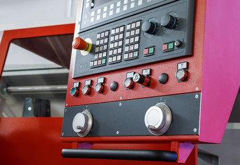 CNC machine control panel with emergency stop button on foreground.