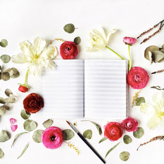 Workspace. Notebook or sketchbook, pink and red roses or ranunculus, white tulips and green leaves on white background. Flat lay, top view