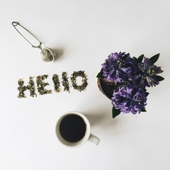 Word "Hello" made with green tea, cup of tea and flowerpot with violet flowers. Isolated on white background. Overhead view