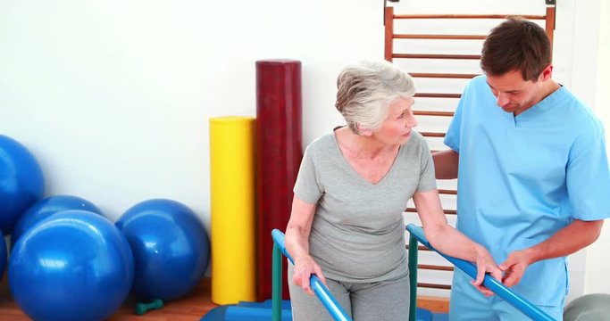 Physical therapist helping patient to walk with parallel bars