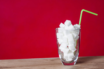 Glass with straw full of sugar and sugar cubes on red background