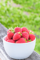 Fresh picked strawberries in white bowl on a wood railing
