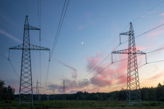 Electricity pylons with wires against the backdrop of the forest and the night sky with the moon.