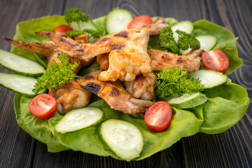 Baked chicken wings with green salad leaves on a wooden table , close-up view.
