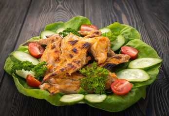 Baked chicken wings with green salad leaves on a wooden table , close-up view.