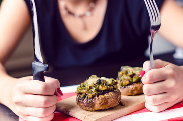 Female hands holding knife and fork and cutting meal. Mushrooms with cheese on a tablecloth. Appetizer. Food background