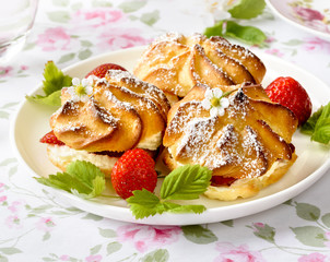 Cream puff cakes or profiterole filled with whipped cream, served with strawberries