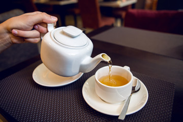 man pours tea from a white teapot in a tea Cup
