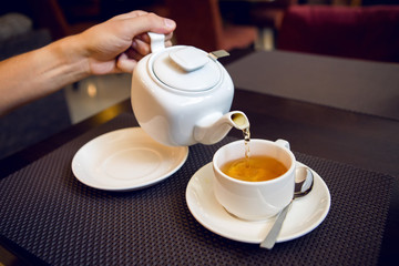 man pours tea from a white teapot in a tea Cup