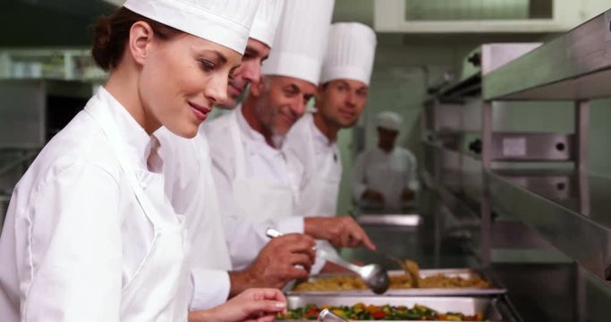Row of chefs preparing food in serving trays