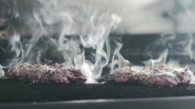 Burger on a grill at commercial kitchen of restaurant. Slow motion.