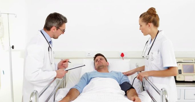 Doctor speaking with sick patient in bed while nurse takes blood pressure