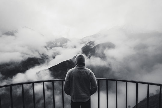 View from behind of a man standing at view point looking to beautiful landscape with foggy mountains in the distance. Black and white photo.