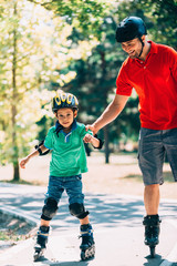 Child roller skating in the park, father helping his confidence