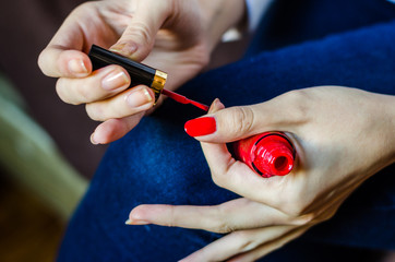 Woman with long fingers painting her long nails with red nail enamel at home, close up photo
