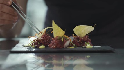 Chef is finishing gourmet meal (raw meat) at commercial kitchen in a restaurant. Close up