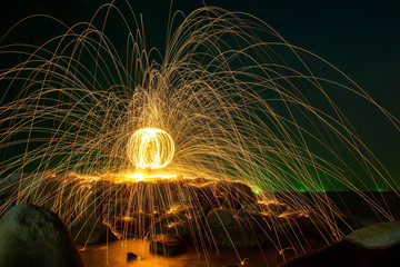 Hot Golden Sparks Flying from Man Spinning Burning Steel Wool into a Sphere on a Rocky Shoreline., Long Exposure Photography using Steel Wool Burning.