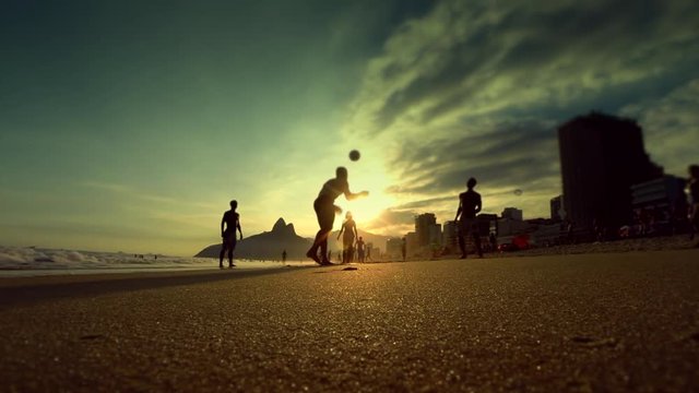 Silhouettes of carioca Brazilians playing altinho beach soccer at sunset on the shore of Ipanema Beach in Rio de Janeiro, Brazil