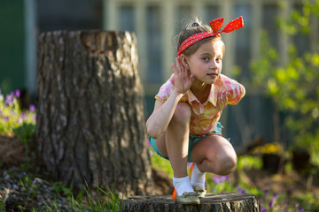 Little naughty girl outdoors, makes the gesture of listening.