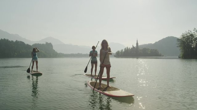 SLOW MOTION: Surfer girls supping on the beautiful lake at sunrise