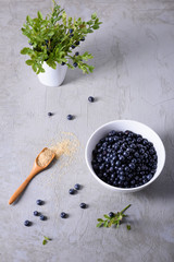 Blueberries in white ceramic bowl with spoon of sugar over grey background. Top view, natural light, copy space.