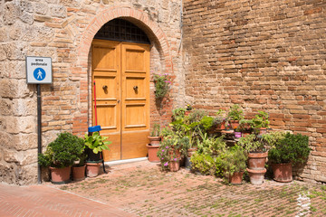 Fototapeta na wymiar Wooden door with flower pots in the medieval tuscan Town San Gimignano