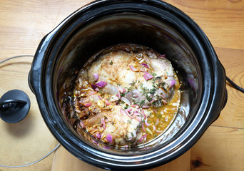 Pulled pork meat cooking in crock pot or slow cooker, with a wooden background. Viewed from above.