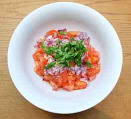 Pico de Gallo Mexican tomato salsa with red onion and cilantro coriander in a white bowl, viewed from above.