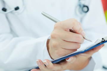 Female medicine doctor hand holding silver pen writing something on clipboard closeup. Ward round, patient visit check, medical calculation and statistics concept. Physician ready to examine patient