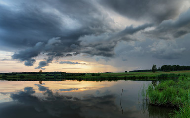 Dramatic summer sunset at the lake with dark clouds before storm